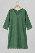 A green cotton tunic top with three-quarter sleeves hangs on a metal hanger against a white wardrobe door.