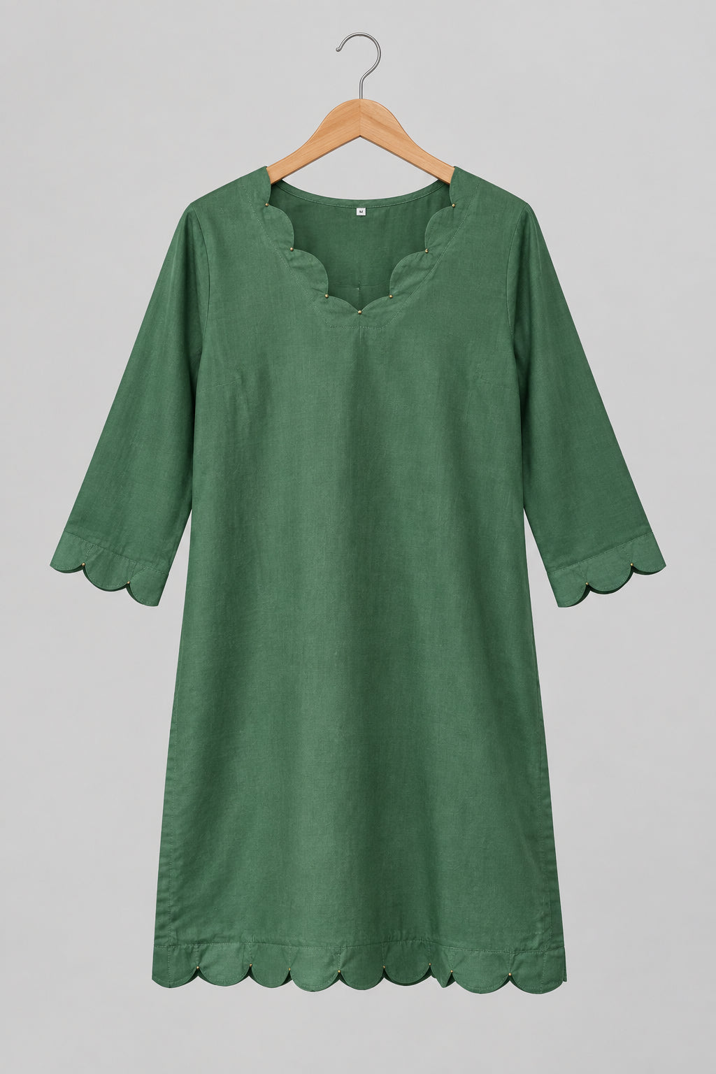 A green cotton tunic top with three-quarter sleeves hangs on a metal hanger against a white wardrobe door.