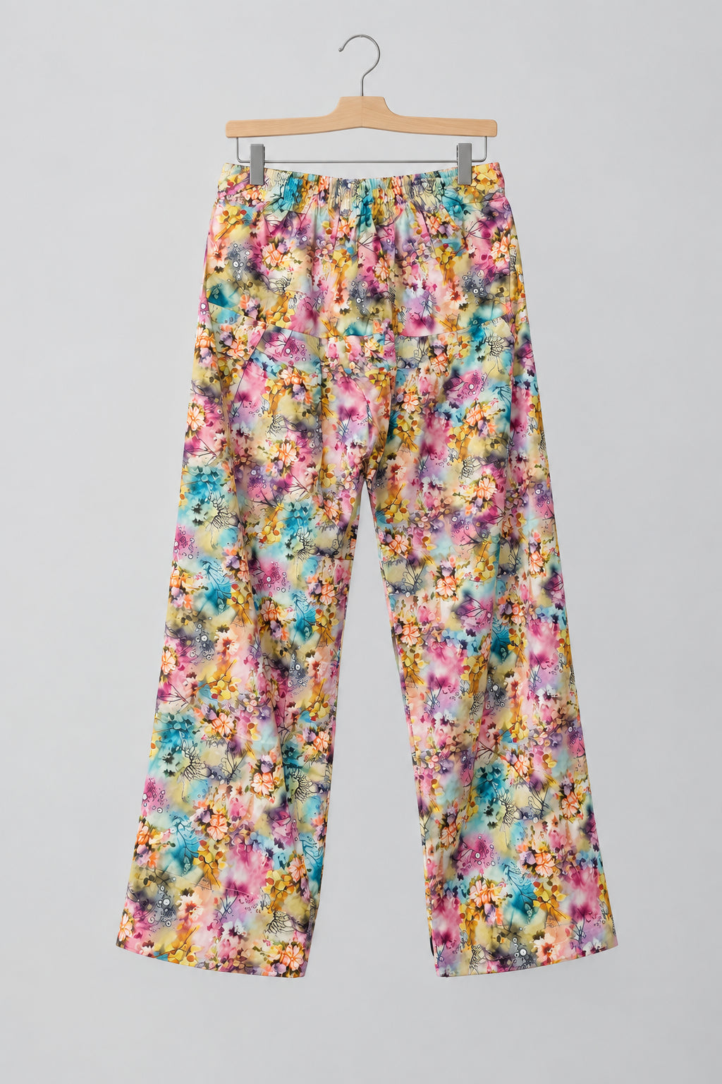 A pair of women's wide-leg pants with a vibrant multicolor floral print, hanging on a metal hanger against a white wardrobe door.