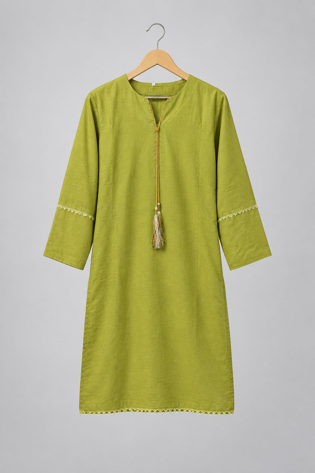 A light olive green tunic dress with three-quarter sleeves and a drawstring tassel, hanging on a black hanger against a white wardrobe door.