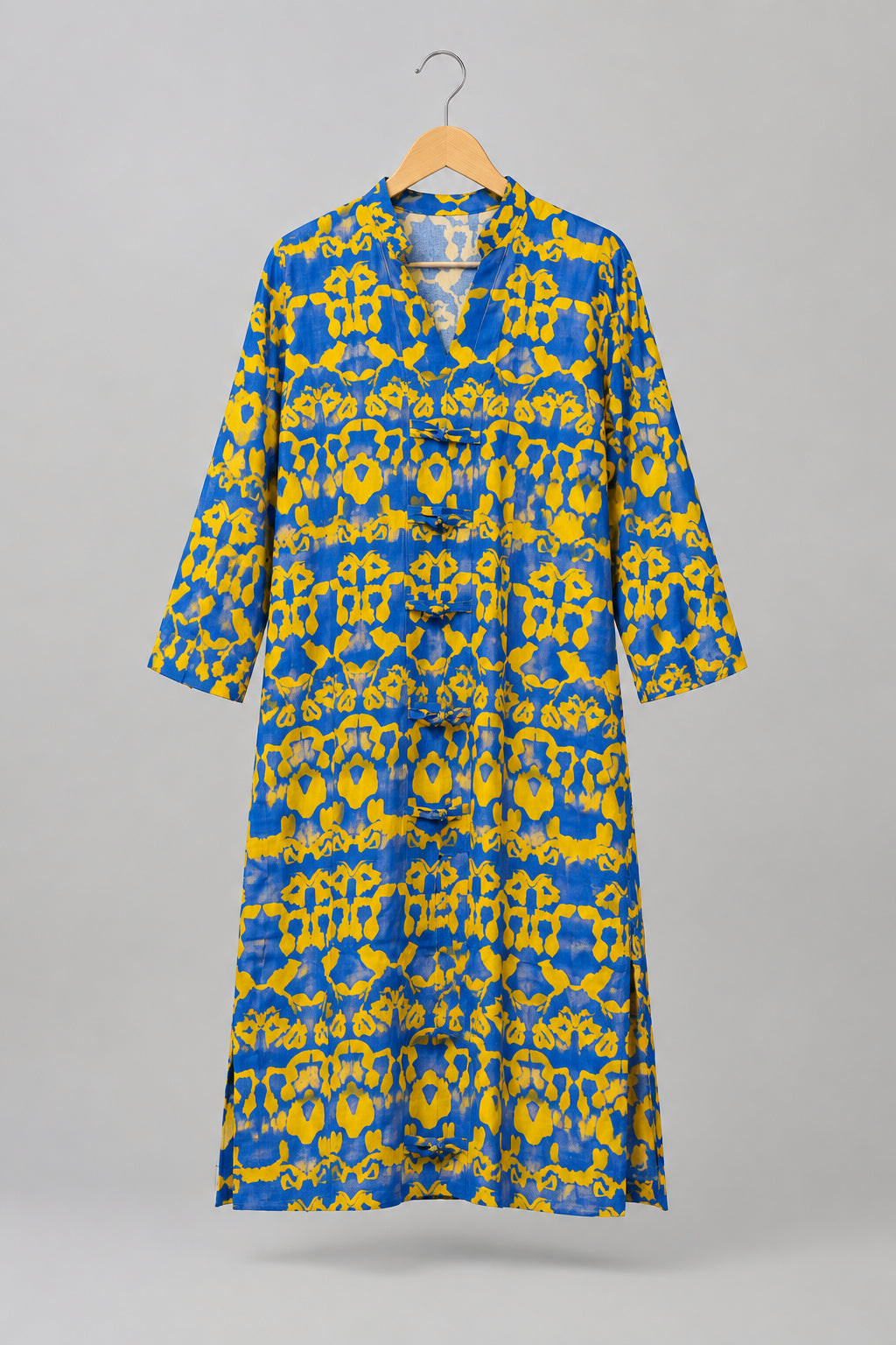 A blue and yellow patterned long-sleeve shirt dress hanging on a metal hanger against a white wardrobe door.