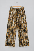 A pair of loose, cropped pants with an abstract black, brown, and white spotted pattern, hanging on a metal hanger against a white wardrobe door.