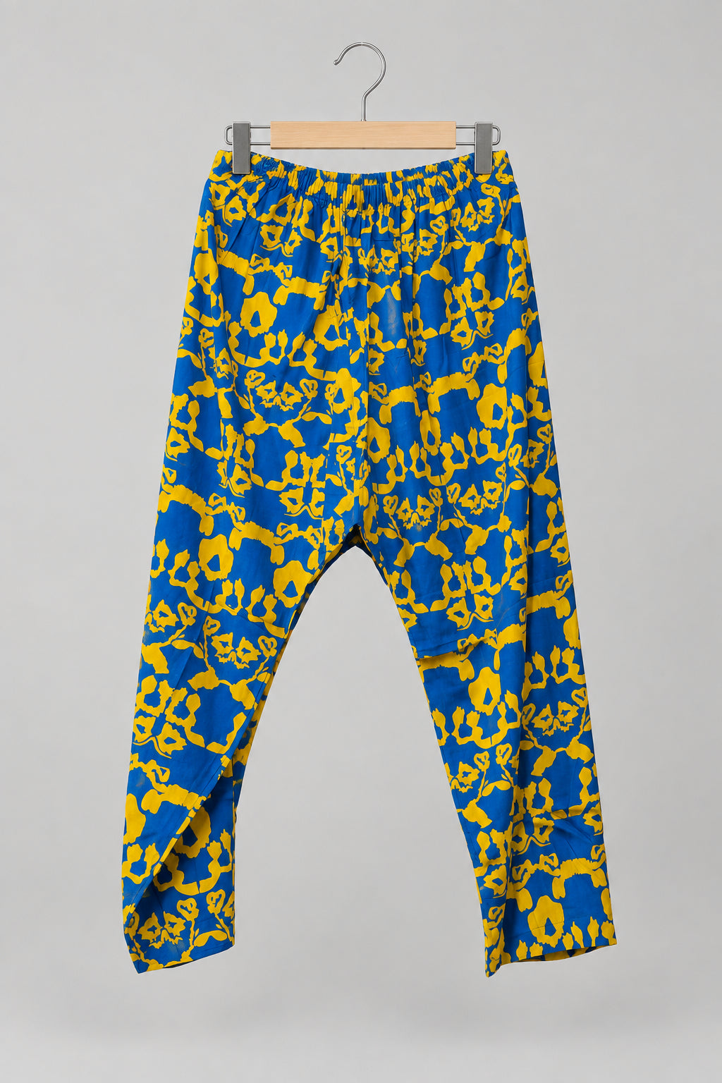 Blue and yellow patterned pants hanging on a metal hanger against a white wardrobe door.