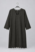 A black three-quarter sleeve tunic top with scalloped edges and decorative beadwork, hanging on a metal hanger against a white wardrobe door.