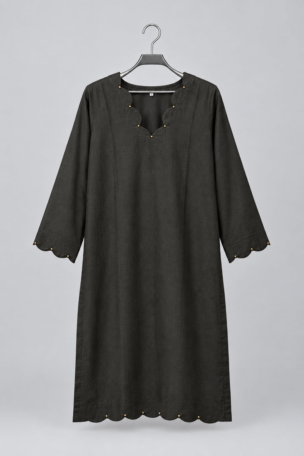 A black three-quarter sleeve tunic top with scalloped edges and decorative beadwork, hanging on a metal hanger against a white wardrobe door.