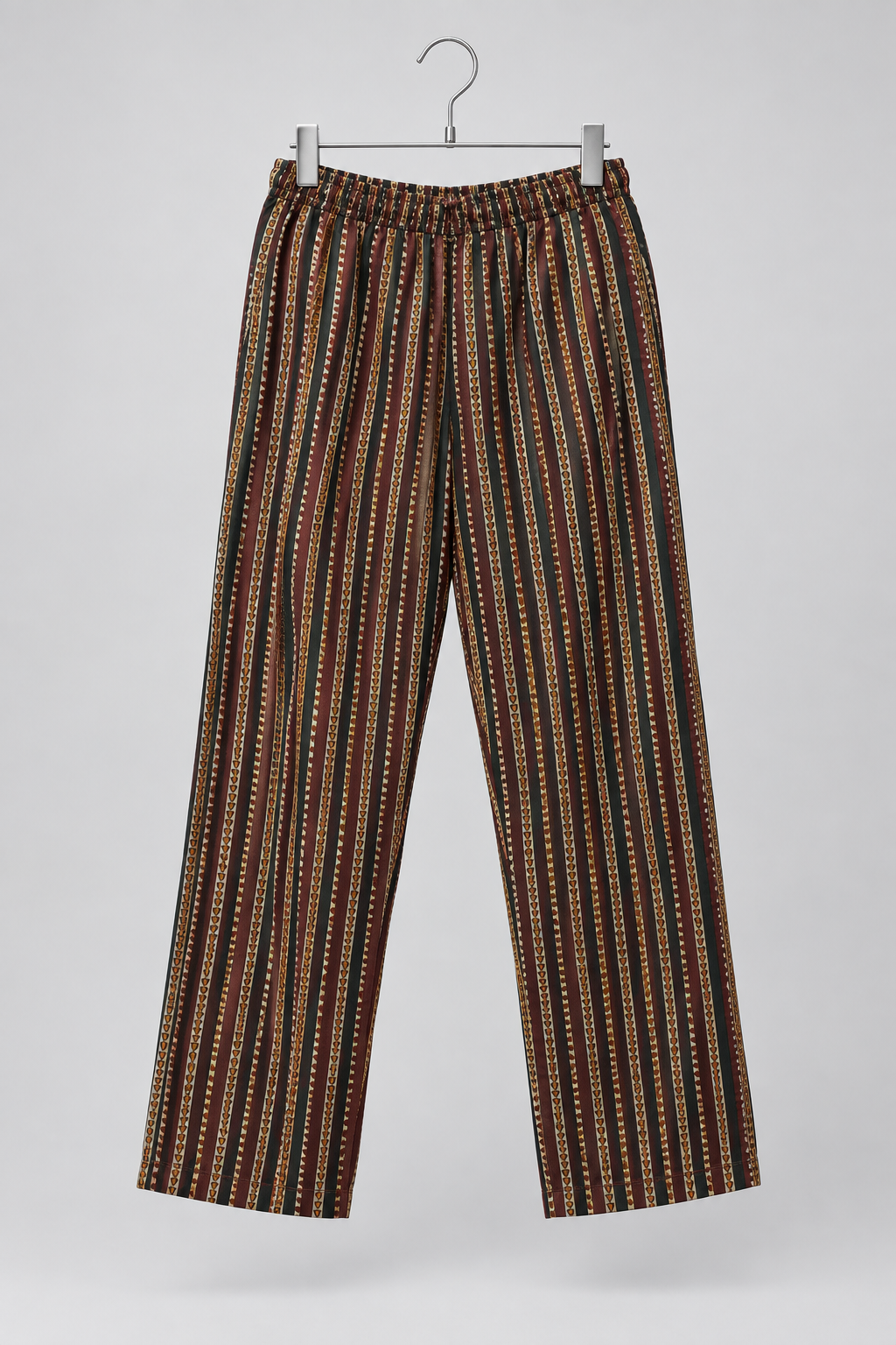 A pair of wide-leg trousers with vertical stripes in brown, beige, and black, hanging from a silver metal hanger against a light gray background.