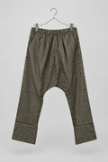 A pair of loose-fitting striped pants hanging on a metal hanger against a white wardrobe door. The pants have vertical black and olive-brown stripes and a gathered elastic waistband.