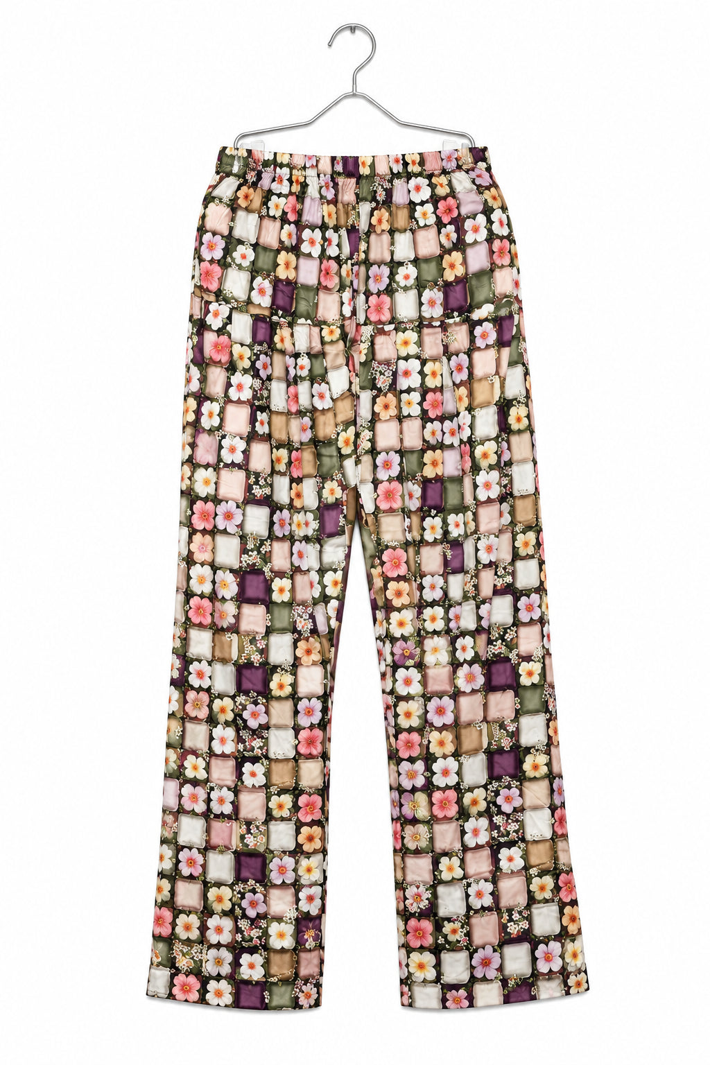 A pair of patterned cropped pants hanging on a metal hanger against a white wardrobe door. The pants feature a busy patchwork-style print with small floral and geometric motifs in pink, purple, green, yellow, and beige tones.