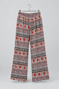 Patterned cropped pants hanging on a metal hanger against a white wardrobe door. The pants feature a busy Nordic/Fair Isle style pattern with red, black, and white.