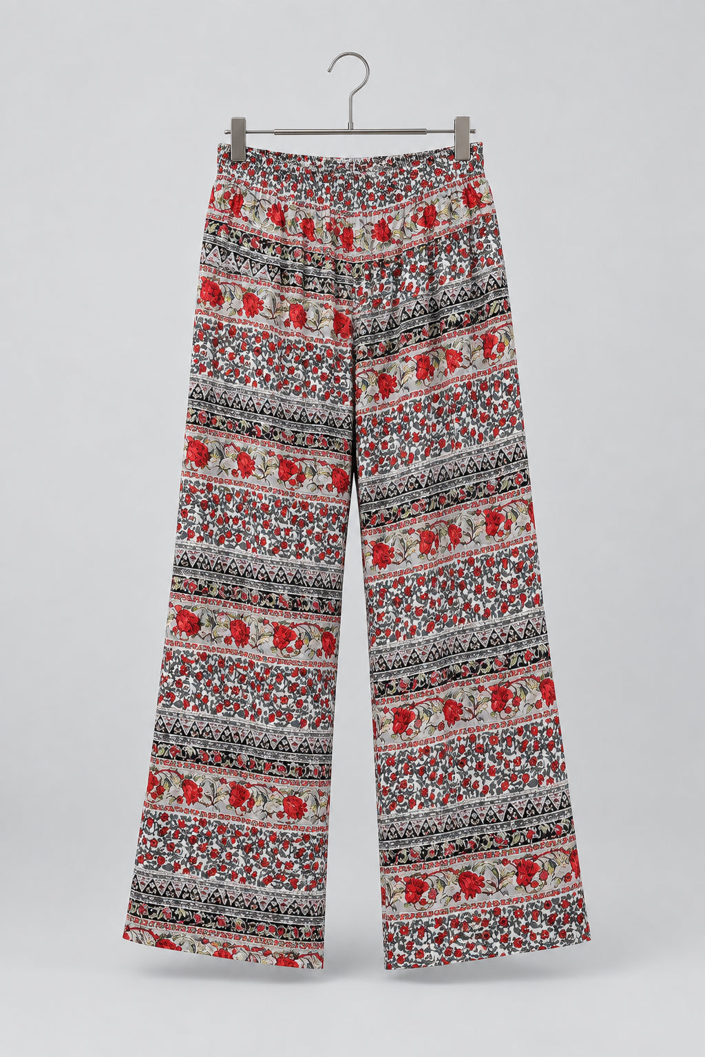 Patterned cropped pants hanging on a metal hanger against a white wardrobe door. The pants feature a busy Nordic/Fair Isle style pattern with red, black, and white.