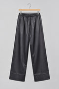 Black wide-leg pants with a drawstring waist, hanging on a metal hanger against a white wardrobe door.