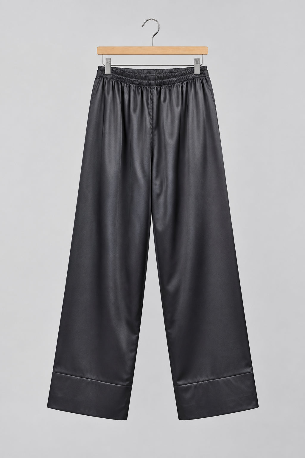 Black wide-leg pants with a drawstring waist, hanging on a metal hanger against a white wardrobe door.